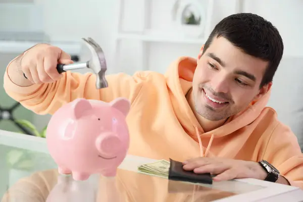 Happy young man with hammer breaking piggy bank at home