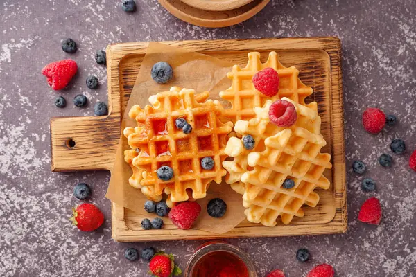 Gri arka planda böğürtlen ve akçaağaç şurubuyla lezzetli waffle tahtaları.