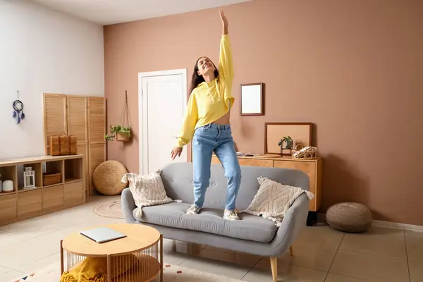 Young woman in hoodie dancing on sofa at home