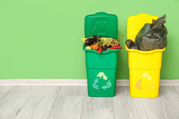 Containers for trash with food waste and full garbage bag near green wall. Recycling concept