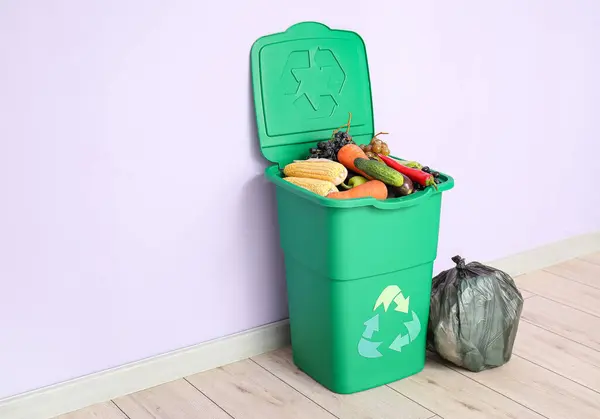 Container for trash with food waste and full garbage bags near lilac wall. Recycling concept