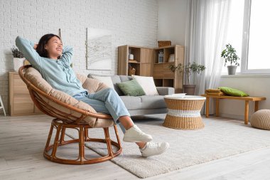 Şık kapüşonlu güzel Asyalı kadın evdeki koltukta oturuyor.