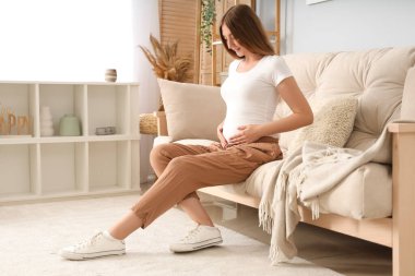 Evdeki kanepede oturan hamile bir kadın.