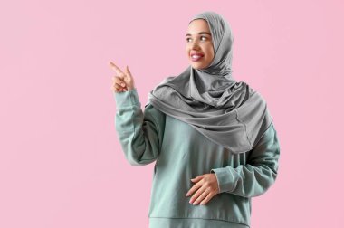 Genç Müslüman kadın pembe arka plandaki bir şeyi işaret ediyor.