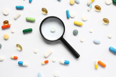 Farklı haplarla dolu balık yağı kapsülleri ve beyaz arka planda büyüteç.