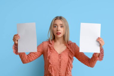 Mavi arka planda boş kağıt çarşafları olan genç bir kadın.