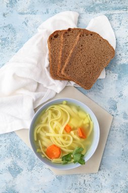 Mavi arka planda bir kase lezzetli tavuk çorbası ve ekmek.