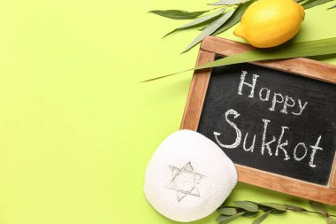 Dört tür (lulav, hadas, arava, etrog), kippah ve yeşil arkaplanda Mutlu SUKKOT yazılı kara tahta