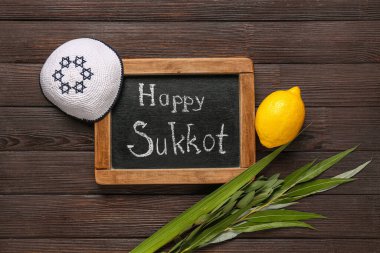 Dört tür (lulav, hadas, arava, etrog), kippah ve tahta zemin üzerinde Mutlu SUKKOT yazılı karatahta