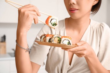 Güzel genç Asyalı kadın mutfakta lezzetli suşi yiyor.