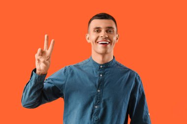 Turuncu arka planda zafer işareti yapan genç adam