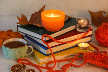 Kitaplar, bir fincan çay, örgü iplikleri ve beyaz arka planda sonbahar yaprakları..
