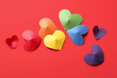 Kırmızı arka planda kağıttan yapılmış renkli kalpler. LGBT kavramı