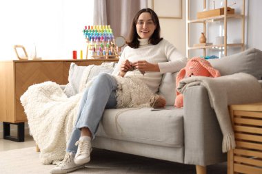 Evde iğnelerle örgü ören genç bir kadın.