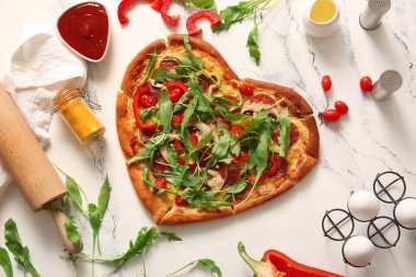 Lezzetli kalp şekilli pizza ve beyaz arka planda malzemeler.