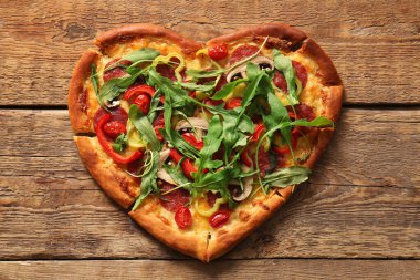 Ahşap zemin üzerinde roka olan lezzetli kalp şeklinde pizza.