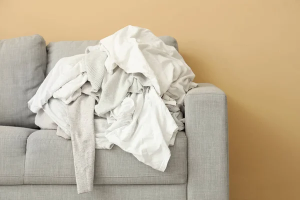 Grey sofa with pile of dirty clothes near beige wall, closeup