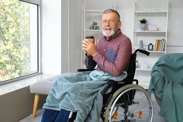 Senior man in wheelchair with cup of coffee at home