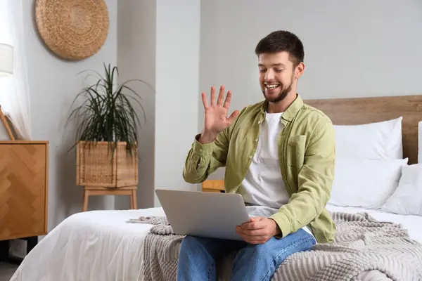 Young bearded man with laptop video chatting in bedroom
