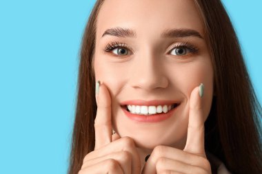 Mavi arka planda sağlıklı dişleri olan gülümseyen genç kadın, yakın plan.