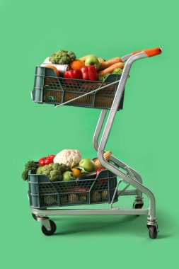 Yeşil arka planda içi taze sebze dolu alışveriş arabası.