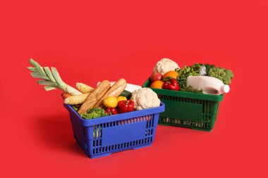 Kırmızı arka planda yiyecek dolu alışveriş sepetleri.