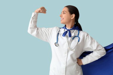Süper kahraman kostümlü güzel bayan doktor mavi arka planda kaslarını gösteriyor.