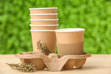 Dekoratif yeşil çimenlere karşı bej ahşap masa üzerinde bitki dalları olan eko sofra takımı