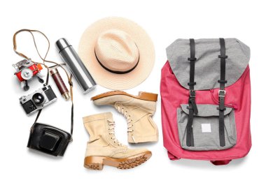 Beyaz arka planda sırt çantası, termos ve fotoğraf makinesi olan gezgin aksesuarları.