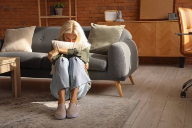 Evde yastıklı depresif olgun bir kadın oturuyor.