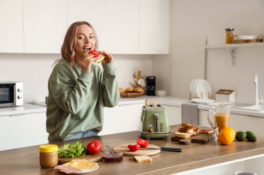 Genç ve güzel bir kadın mutfakta lezzetli bir sandviç yiyor.
