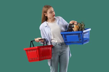 Yeşil arka planda boş ve dolu alışveriş sepetleri olan genç bir kadın. Fiyat artışı kavramı