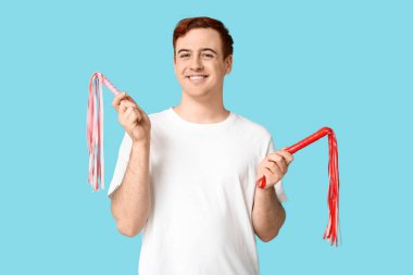 Mavi arka planda kırbaçları olan yakışıklı bir genç.