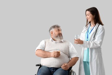 Tekerlekli sandalyedeki olgun adam, haplar ve arka planda hemşire.