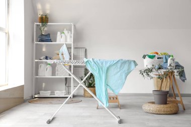 Çamaşır odasındaki ütü masasında elektrikli ütü ve buruşuk gömlek.