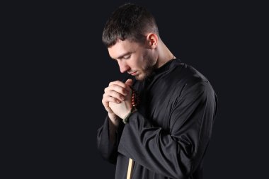 Genç rahip siyah arkaplanda boncuklarla dua ediyor.