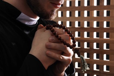 Günah çıkarma kabininde dua eden genç rahip, yakın plan.