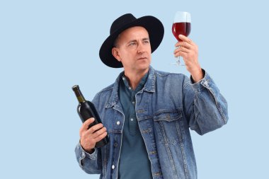 Mavi arka planda cam ve kırmızı şarap şişesi olan olgun bir adam.