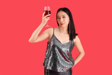 Kırmızı arka planda bir bardak şarabı olan güzel bir Asyalı kadın.