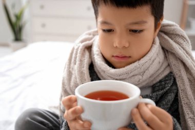 Yatak odasında çay içen küçük Asyalı çocuk, yakın plan.