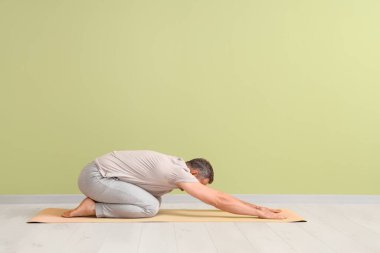 Olgun adam yeşil duvarın yanında yoga yapıyor.
