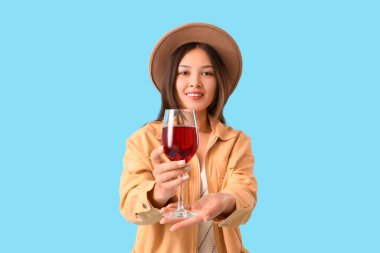 Mavi arka planda kırmızı şarap kadehi olan genç Asyalı kadın.