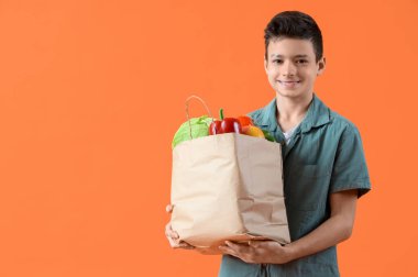 Turuncu arka planda farklı sebzelerle dolu kese kağıdı tutan sevimli bir çocuk.