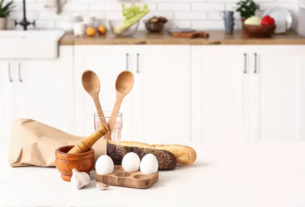 Eggs, fresh bread and cooking utensils on table in kitchen