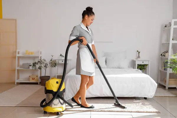 Pretty chambermaid cleaning hotel room with vacuum cleaner