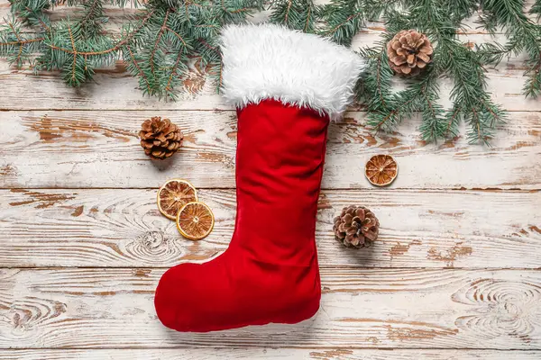 Noel çorabı, köknar dalları, koniler ve beyaz ahşap arka planda kurutulmuş portakal.