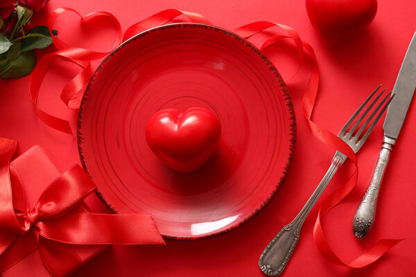 Красивая сервировка стола с розами и подарком на День Святого Валентина на красном фоне
