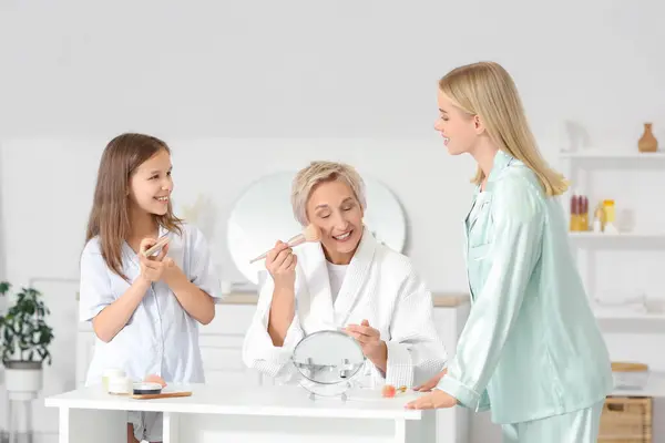 Little girl with her mom and grandmother doing makeup in bathroom