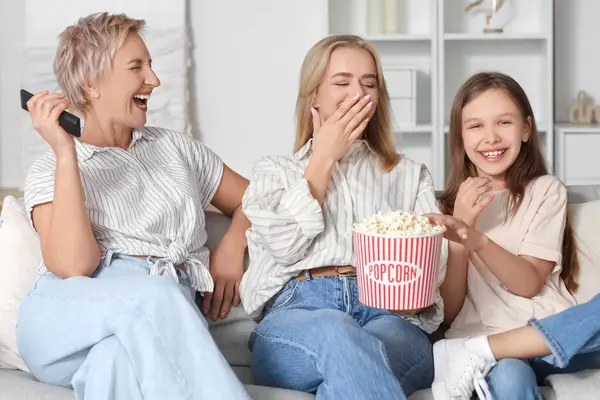 Little girl with her mom and grandmother watching movie at home