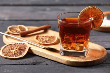 Lezzetli bir bardak eski moda kokteyl ve siyah ahşap arka planda portakal dilimleri.